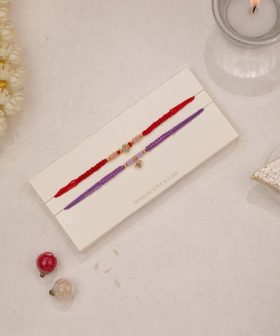 Gold-tone Rakhi with clear stones and pink beads on red thread, and purple thread with square charm