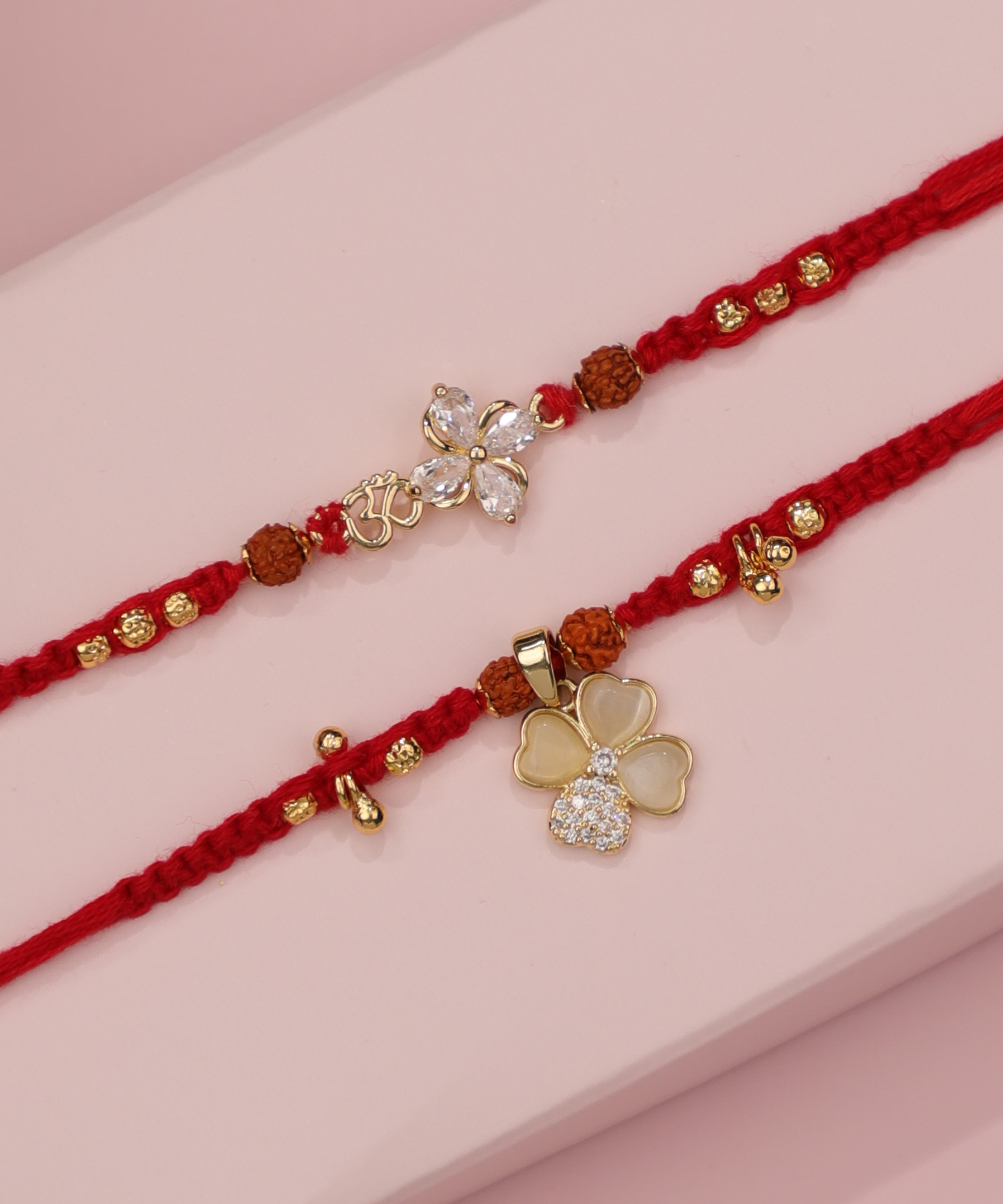 Gold-tone Rakhi set with CZ floral charm, Om symbol, and faux opal clover design on red thread.