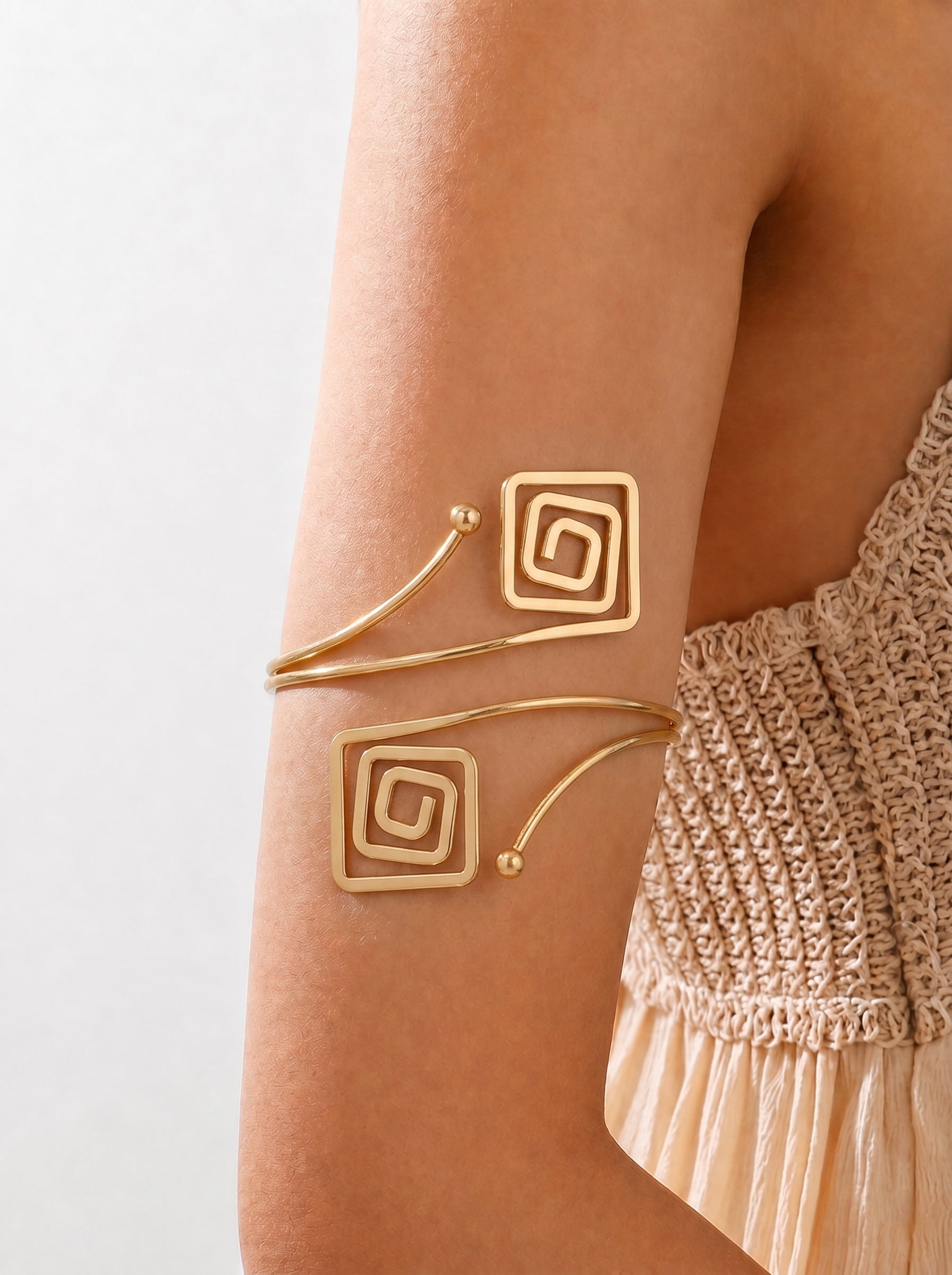 Gold arm cuff with spiral design on a person's arm against a neutral background