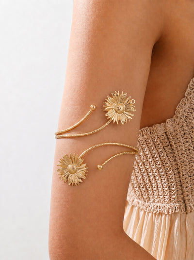 Gold arm cuffs with floral designs on a person wearing a beige top against a light background