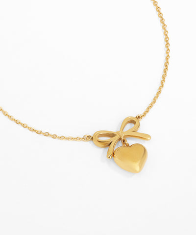 Gold necklace with a heart and bow pendant on a white background