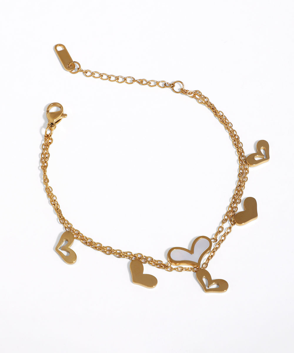 Gold-tone double chain bracelet with various heart charms, one featuring a white shell-like inlay
