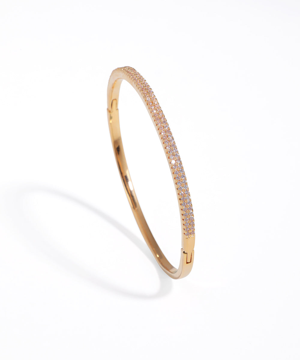 Gold-tone bangle bracelet with two rows of clear stones on upper half and a hinge clasp