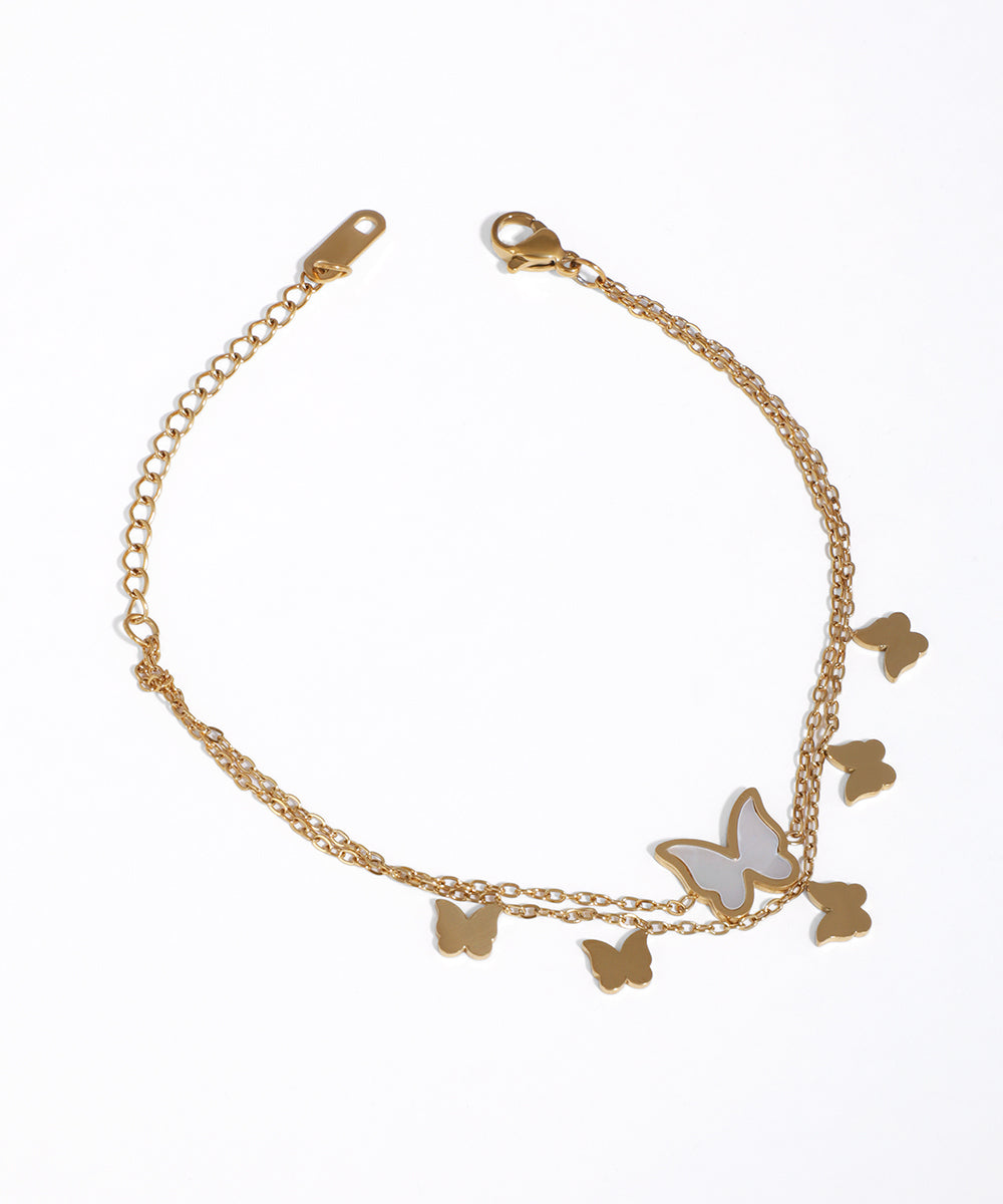 Gold-tone layered bracelet with multiple butterfly charms, one featuring a white iridescent inlay and a lobster clasp.