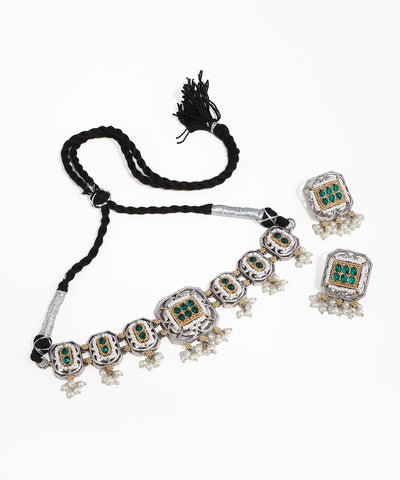 Ornate necklace with emerald green stones and tassel on a white background
