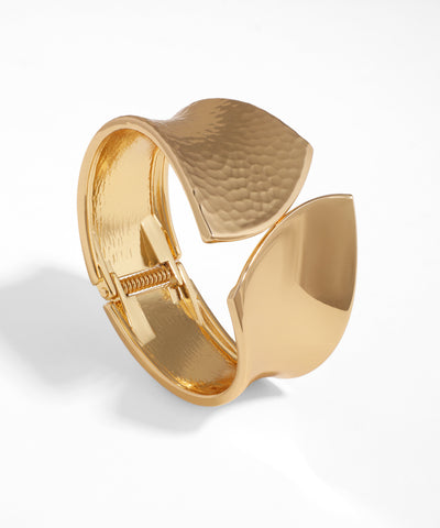 Gold-tone bangle bracelet with wide sculptural wavy design, featuring both hammered and smooth textures.