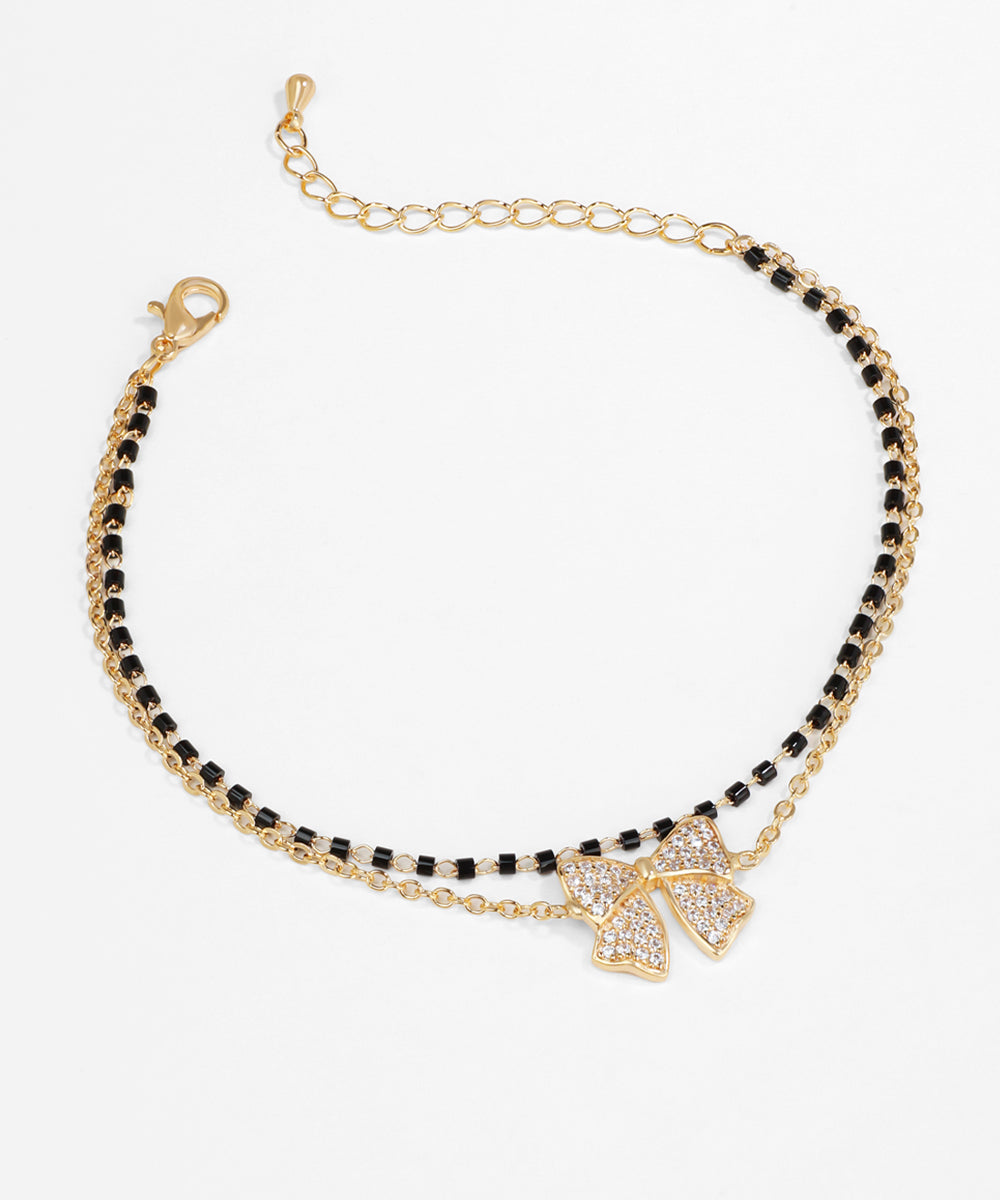 Bracelet with black beads and gold bow charm on a white background