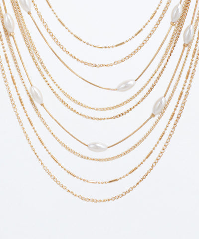 Gold chain necklace with white beads on a light gray background