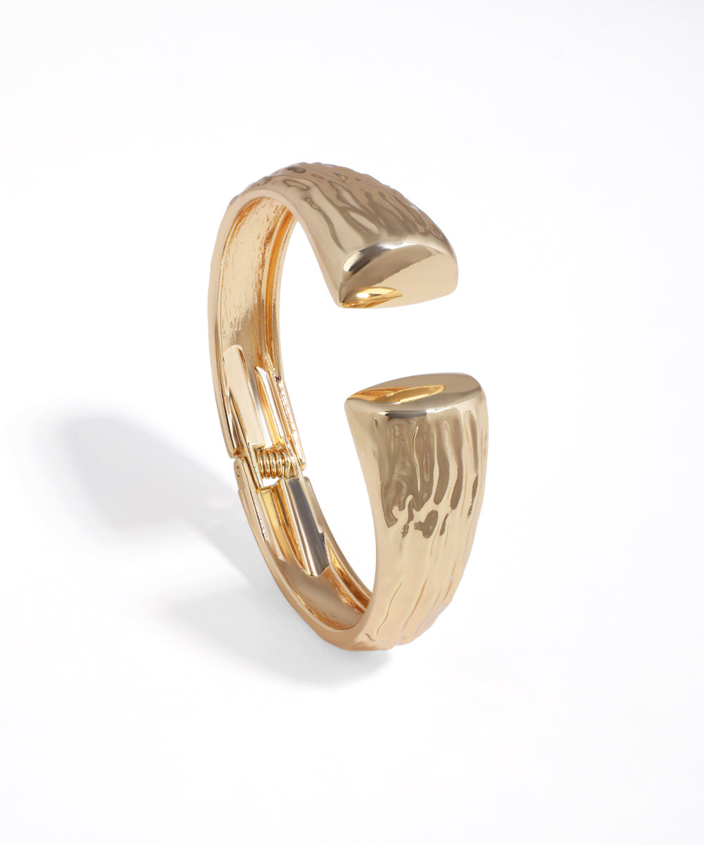 Gold-tone bangle bracelet with a sculpted, open design and textured finish