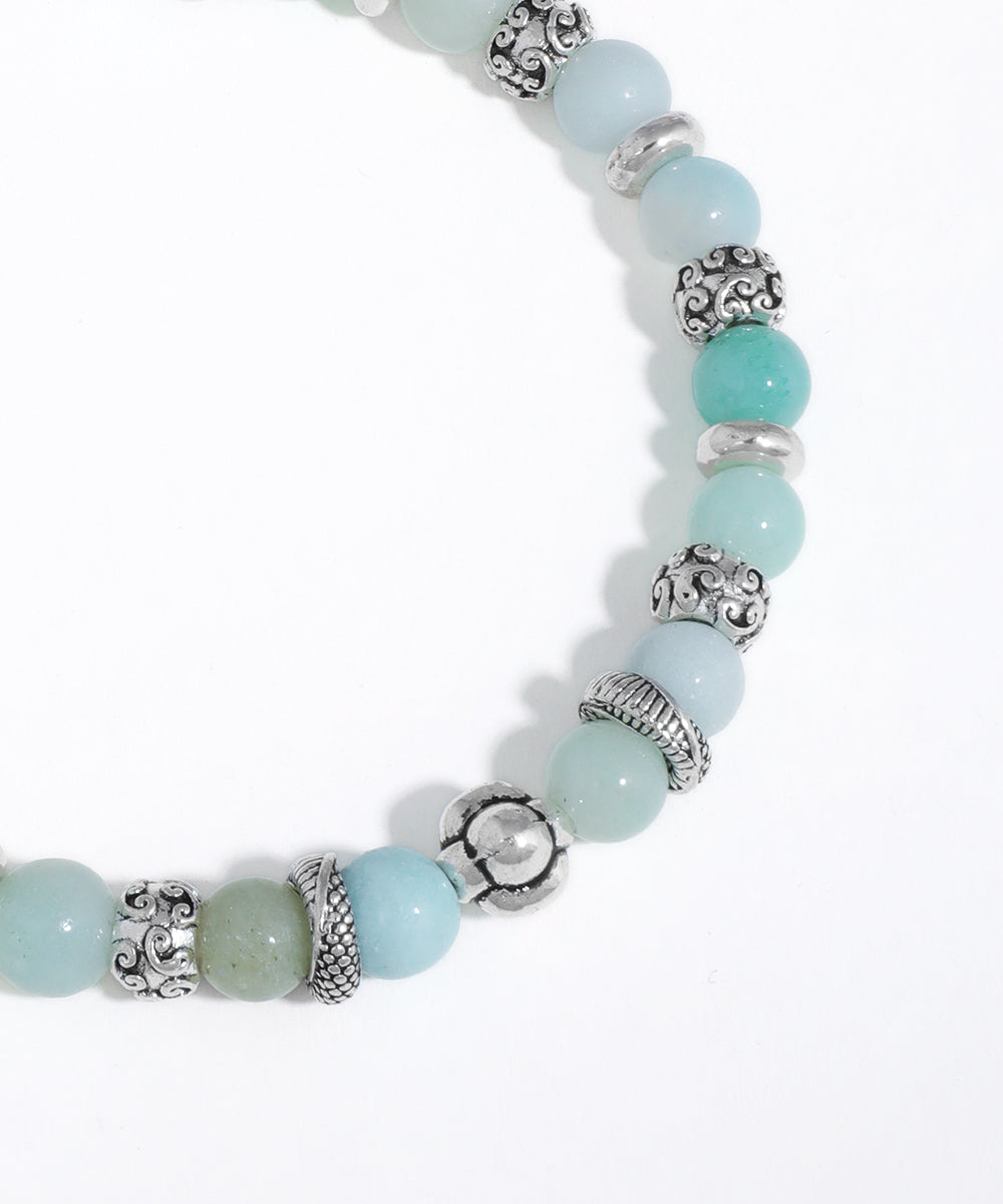 Beaded bracelet with light blue beads and silver charms on a white background