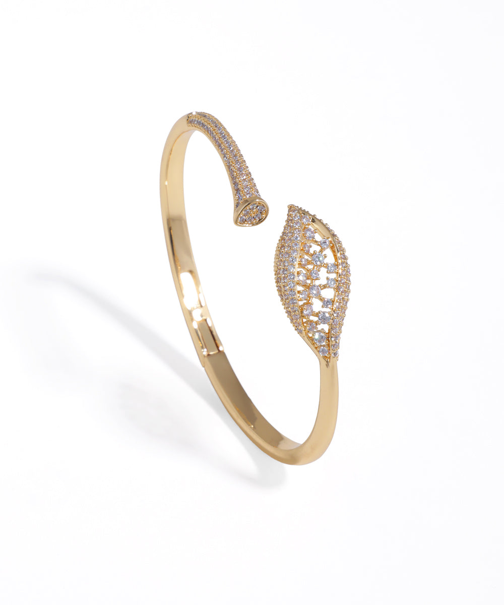 Gold-tone open cuff bracelet with pave-studded leaf and tapered ends on a white background