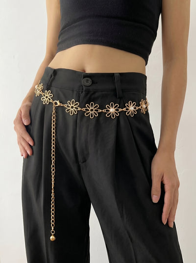 Person wearing black pants with a gold chain belt featuring floral designs on a plain background
