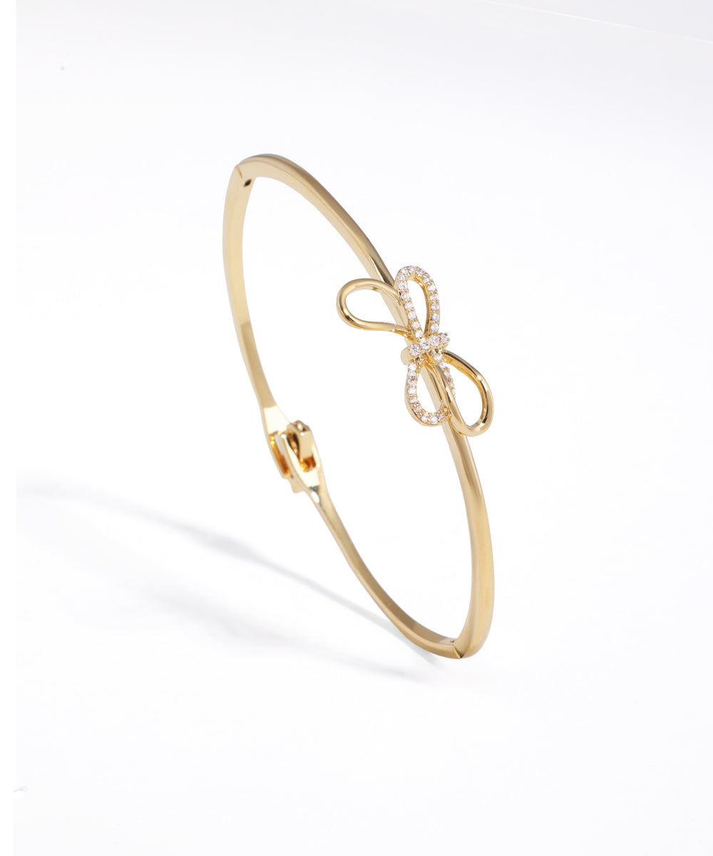 Gold-tone hinged bracelet with a sparkling CZ-studded bow motif