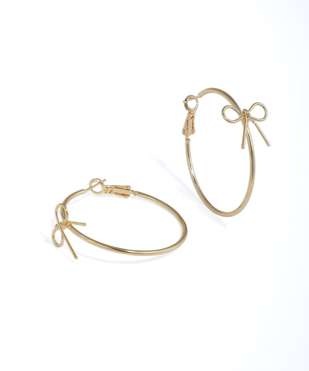 Gold hoop earrings with bow details on a white background
