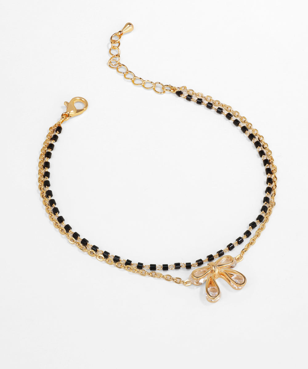 Gold and black beaded bracelet with a bow charm on a white background