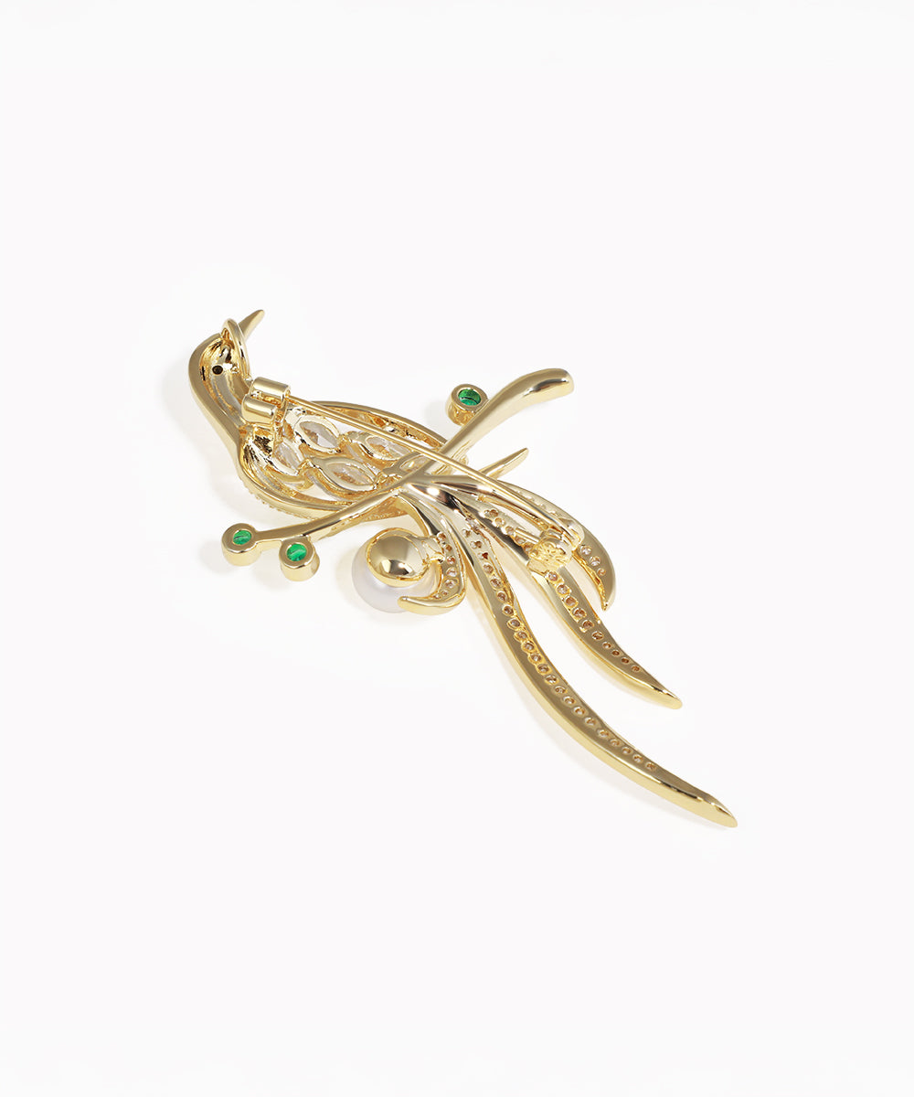 Gold peacock-shaped brooch with green gemstones on a white background
