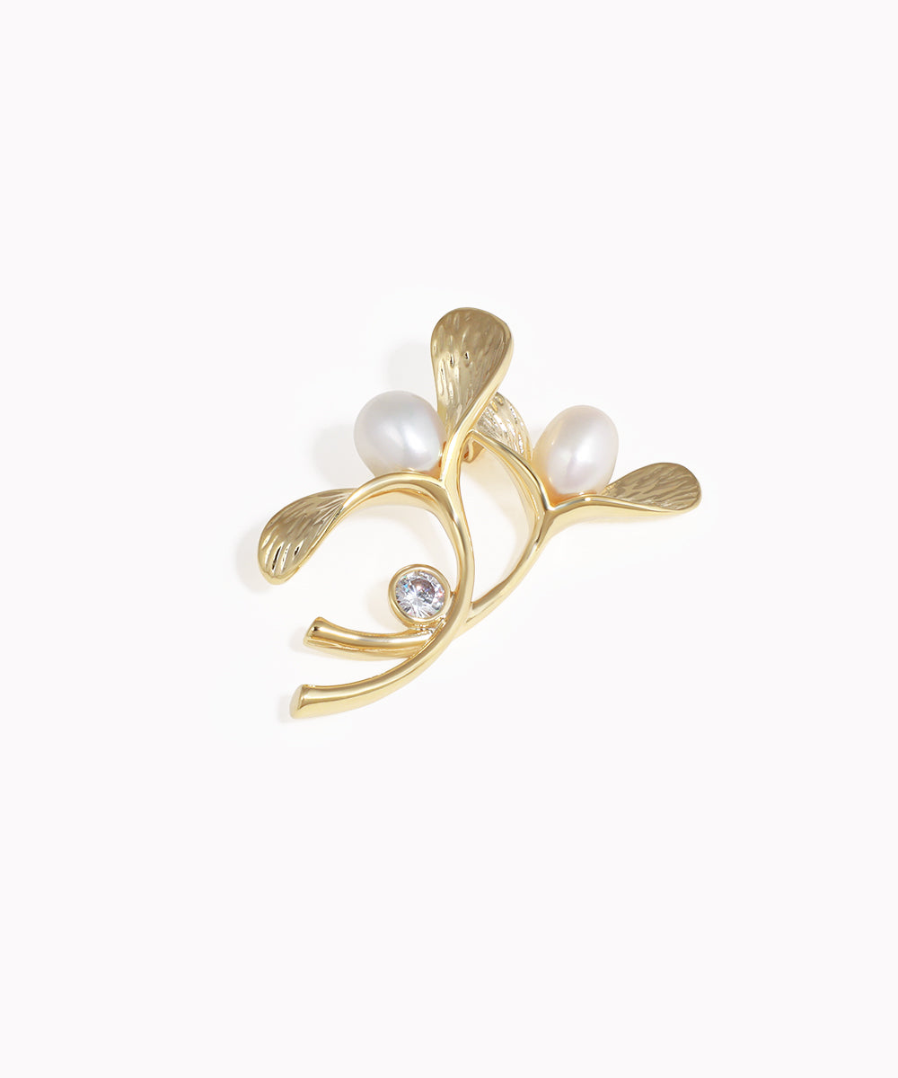 Gold leaf-shaped earring with pearls and a gemstone on a white background