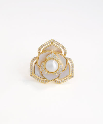 Gold ring with a central pearl and diamond-studded design on a white background
