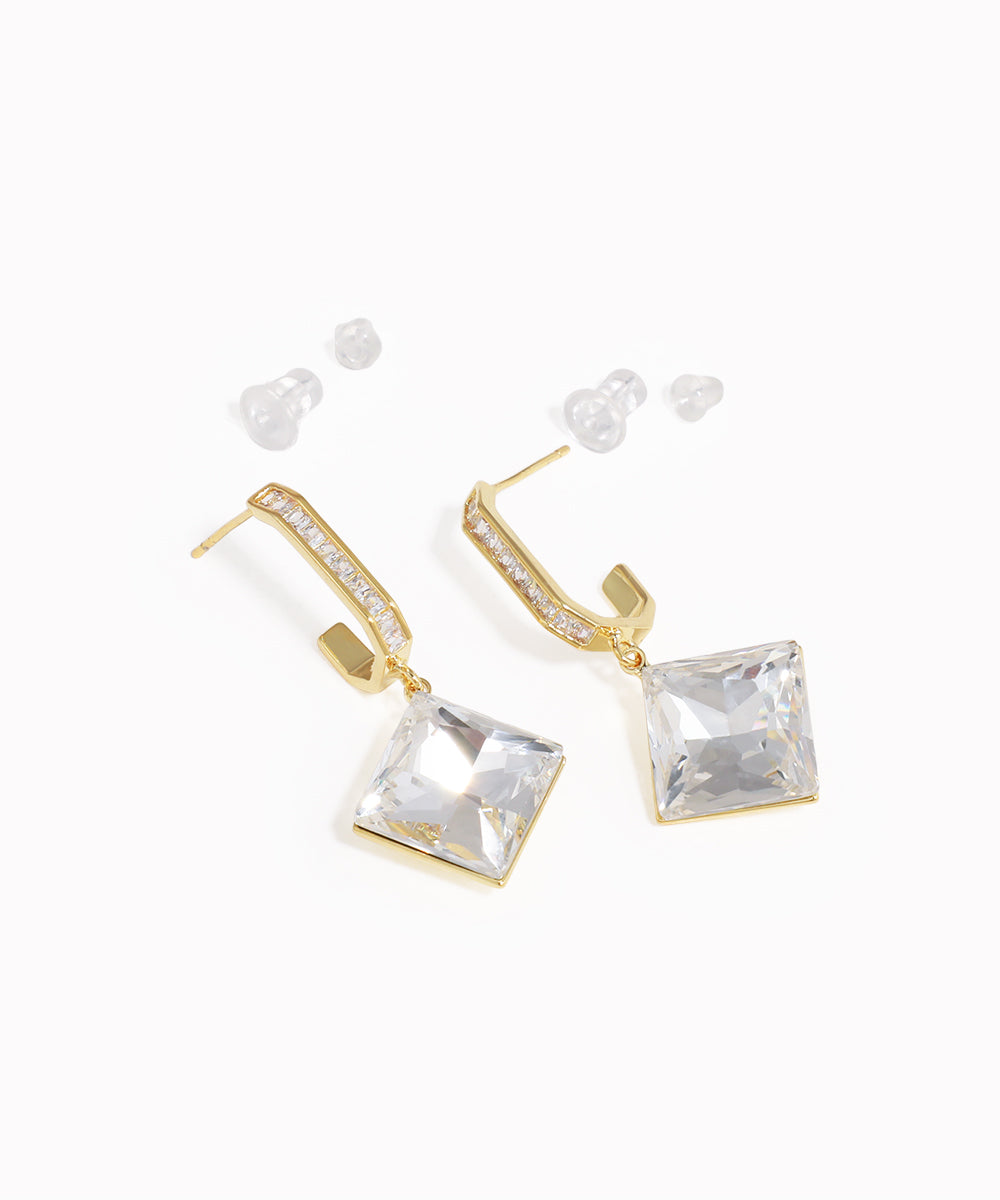 Gold earrings with clear square stones on a white background