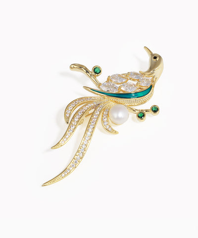 Gold peacock-shaped brooch with pearls and emeralds on a white background