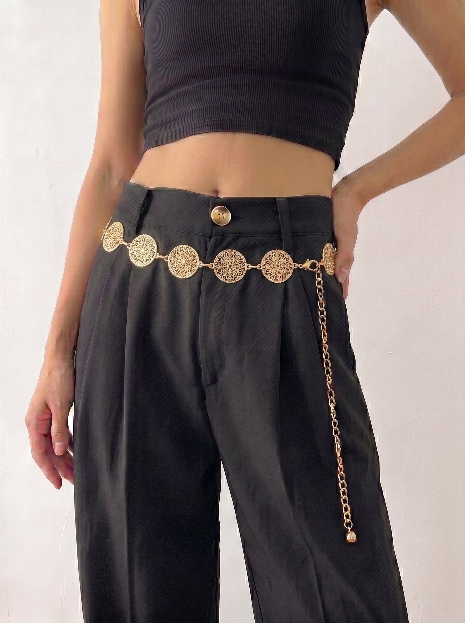 Person wearing black pants with a gold belt featuring circular designs on a white background