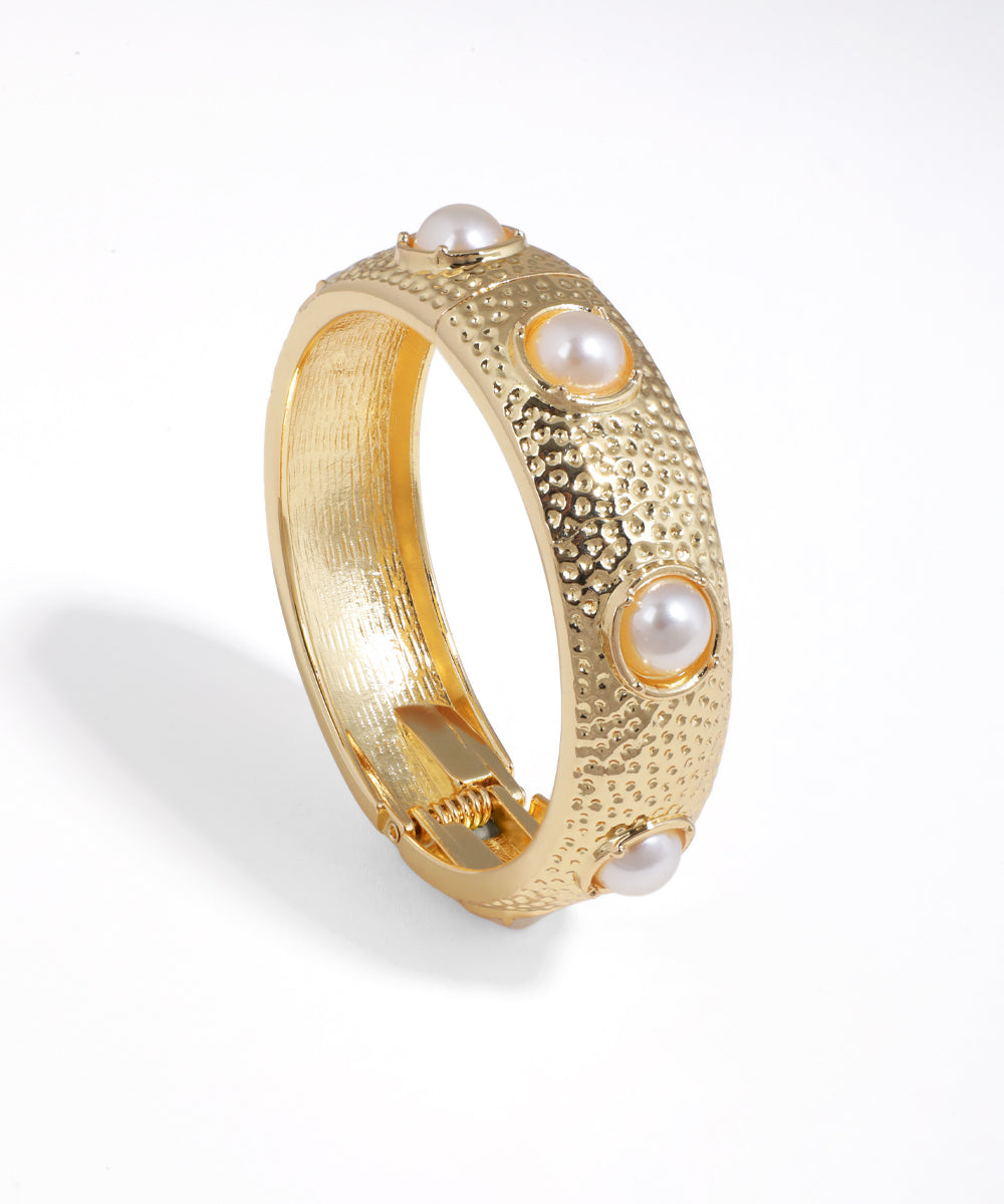 Gold-tone bangle bracelet with hammered texture and faux pearl dome details