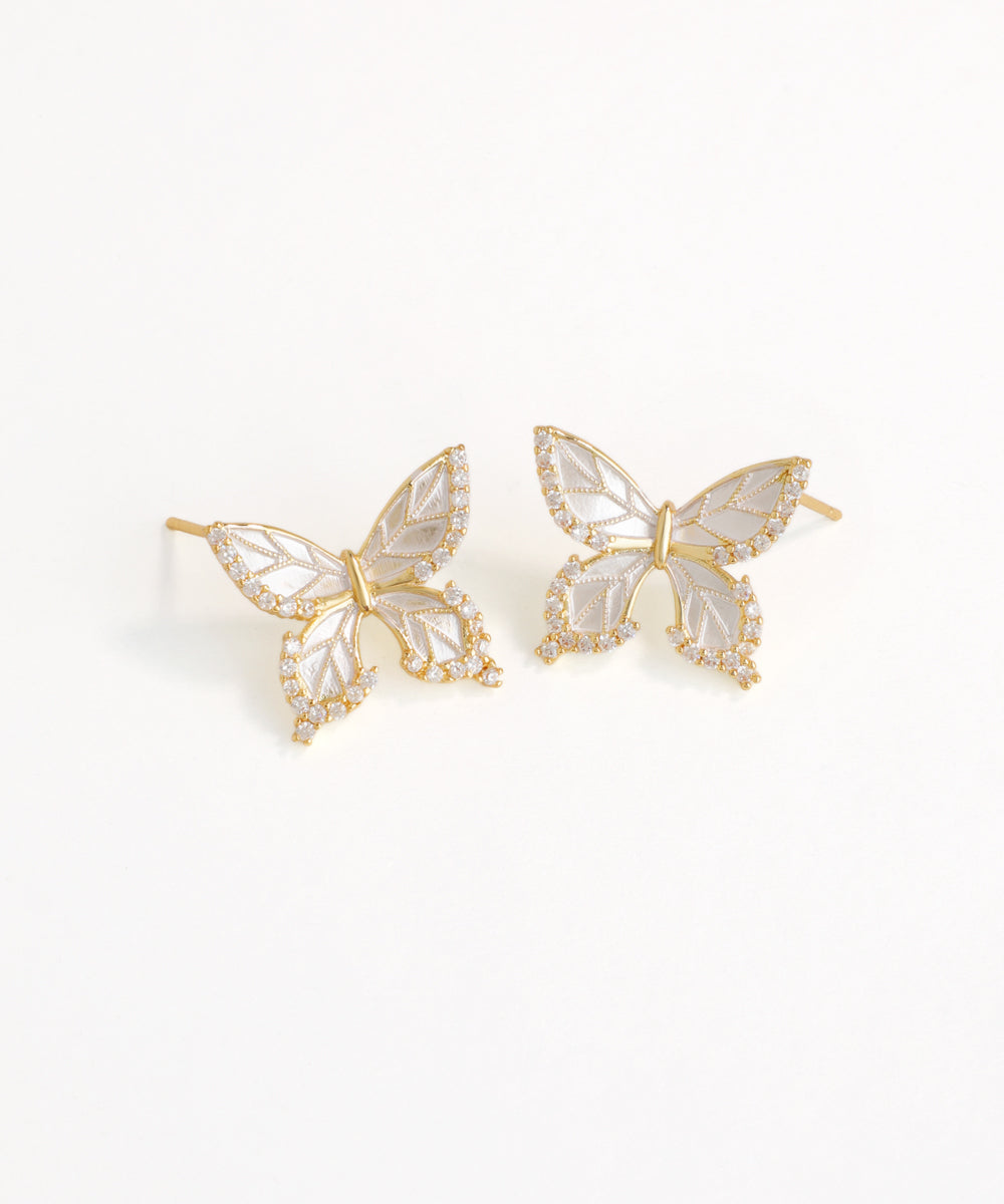 Butterfly-shaped earrings with gold and white design on a light background