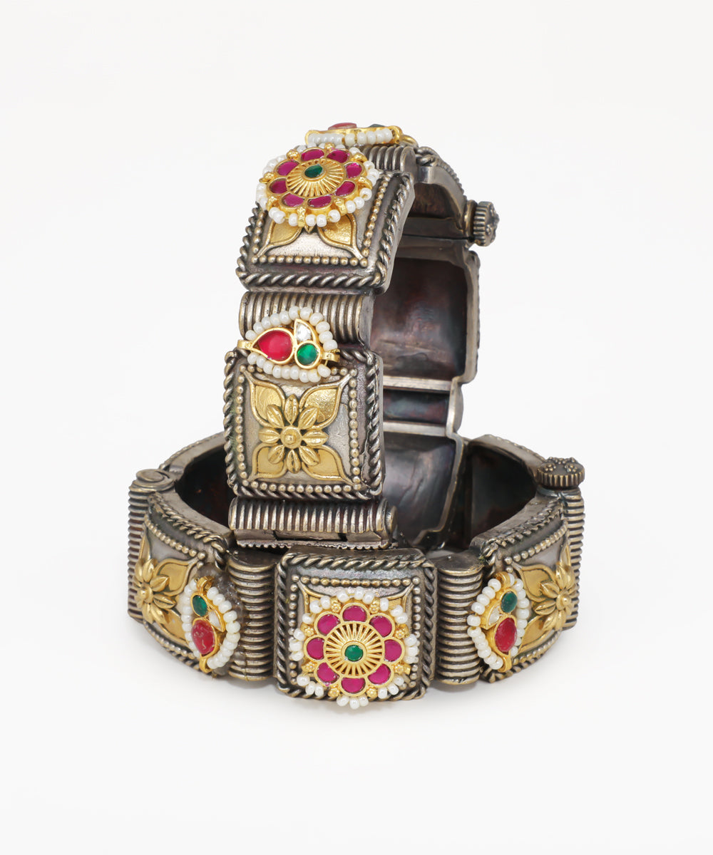 Decorative silver bracelet with floral designs and colored stones on a white background