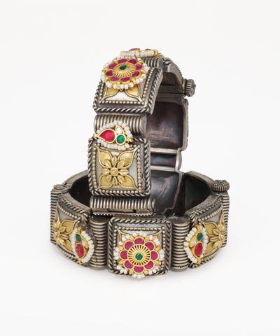 Decorative silver bracelet with floral designs and colored stones on a white background