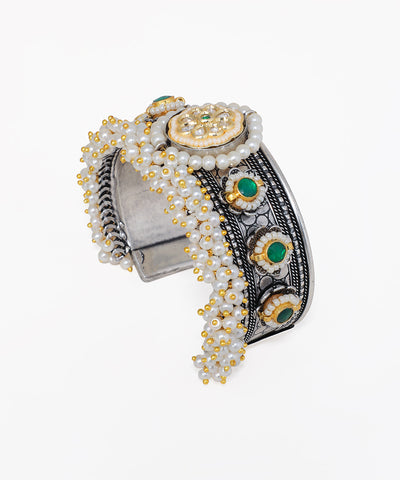 Decorative bracelet with pearls, gold accents, and green stones on a white background