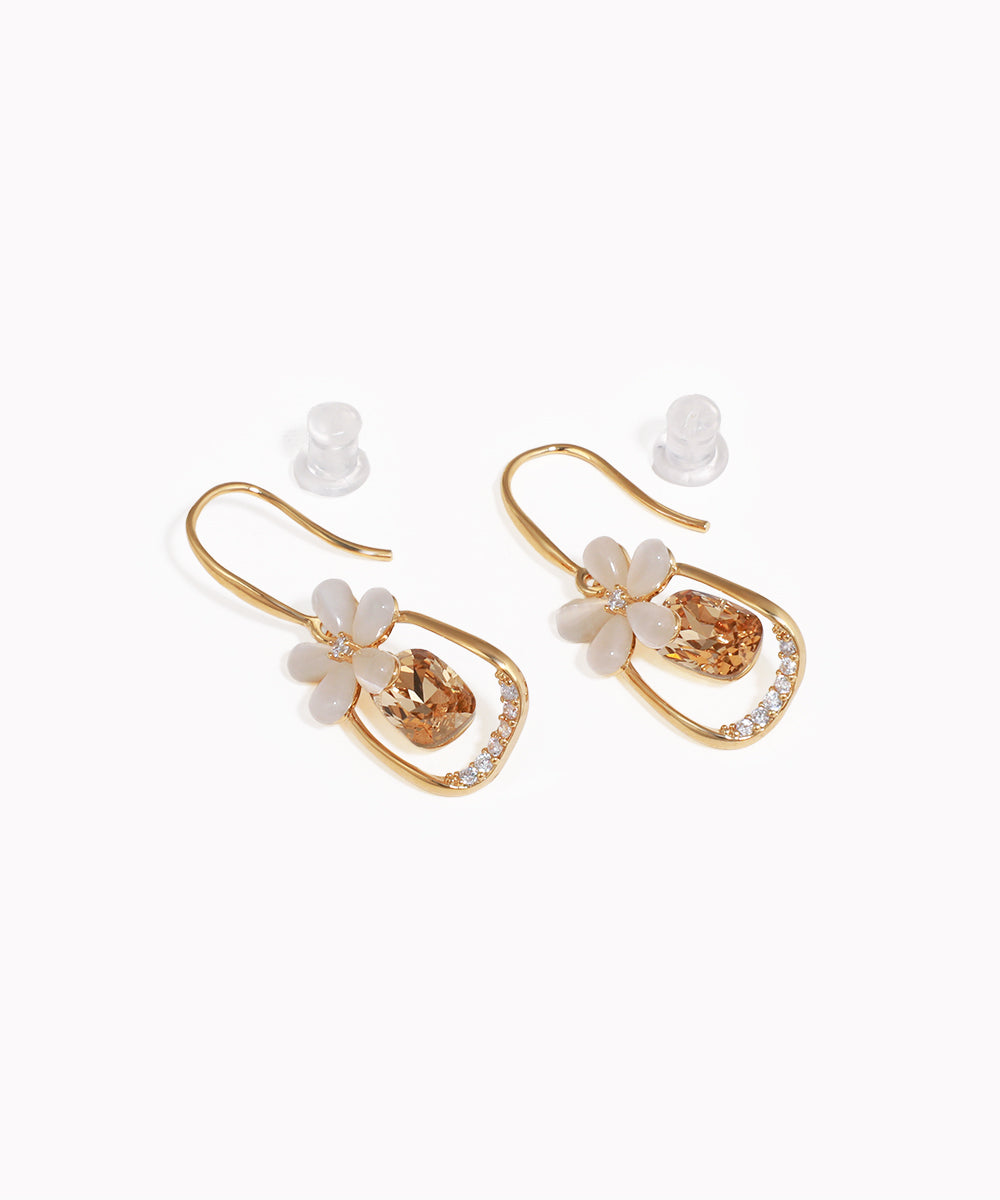 Gold-tone drop earrings with white flower petals, amber glass crystal, and clear CZ stones lining the frame