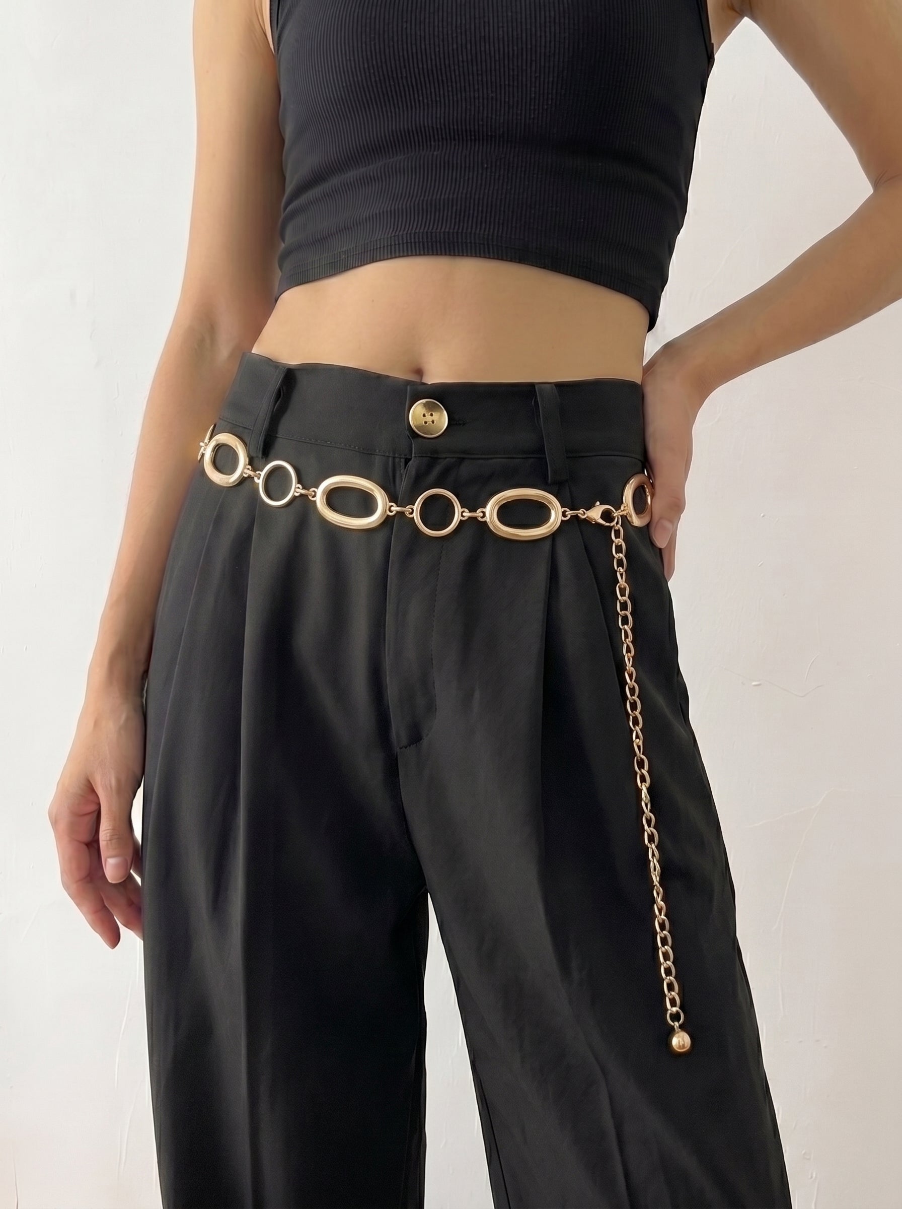 Person wearing black pants with a gold chain belt on a white background