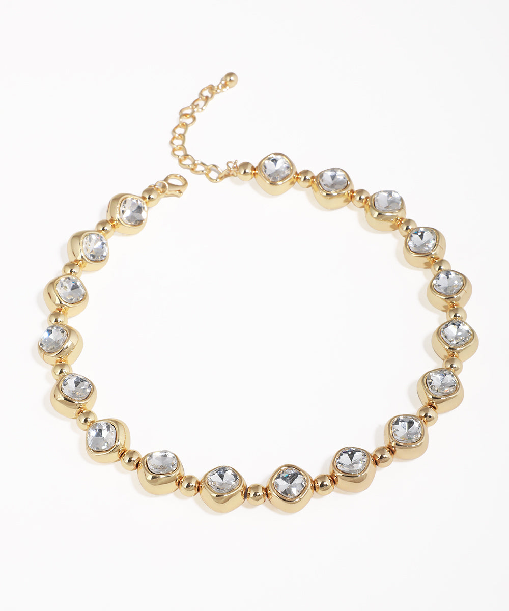 Gold-tone necklace with clear bezel-set stones and small round beads, featuring a lobster clasp closure