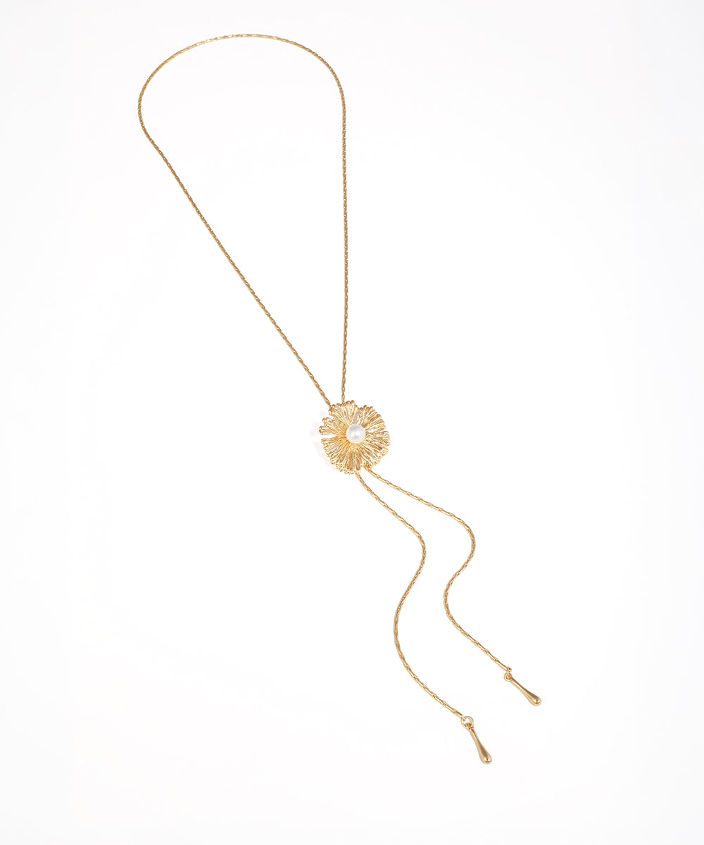 Gold-tone necklace with textured floral motif and faux pearl center, featuring adjustable lariat chains.