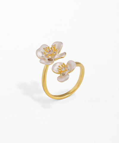 Gold-tone ring with two white floral motifs and clear CZ stones.