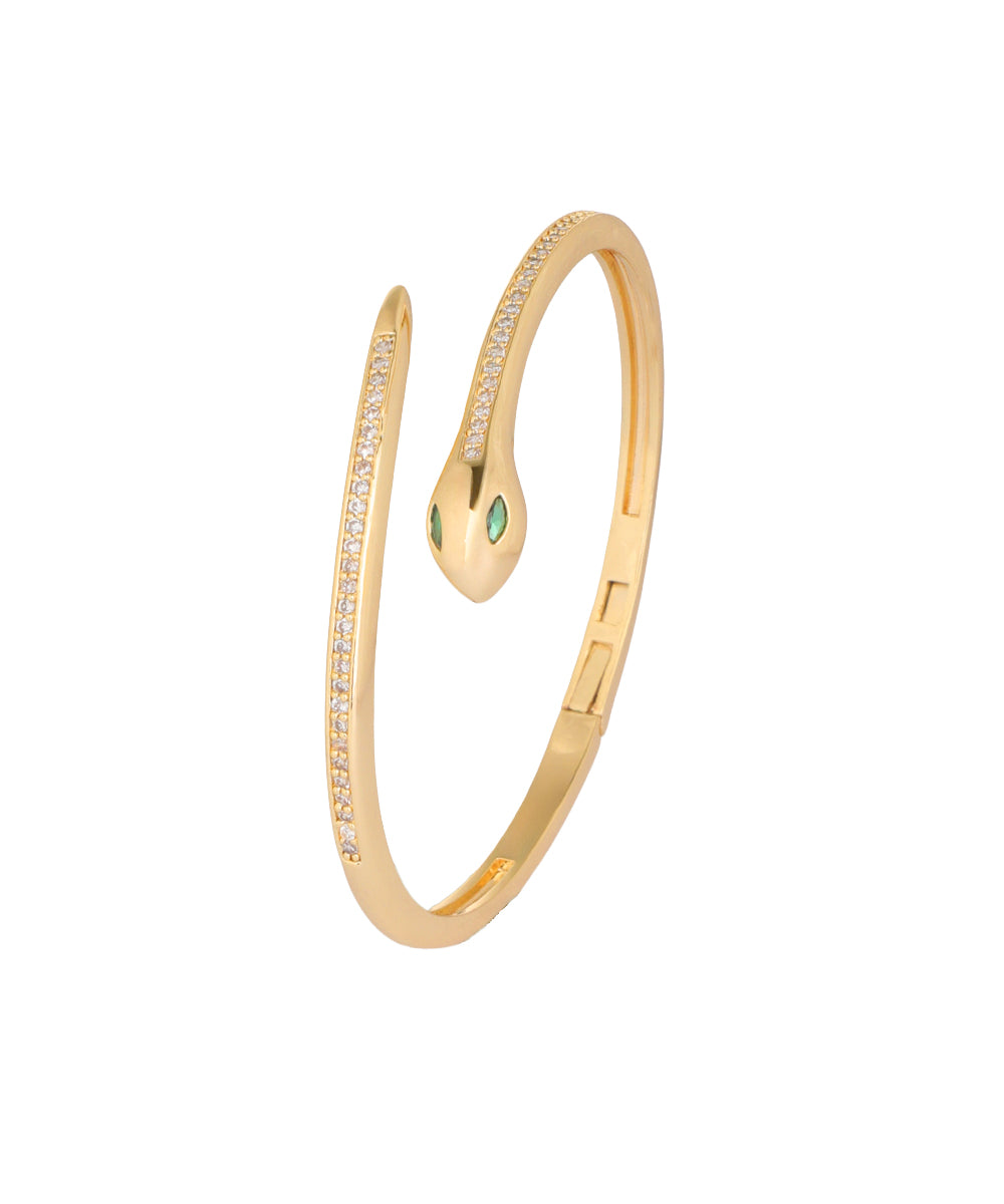 A gold snake-shaped cuff bangle bracelet with small clear pavé stones along the body and two green emerald-cut gemstones at the head, shown on a plain white background.