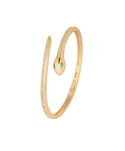 A gold snake-shaped cuff bangle bracelet with small clear pavé stones along the body and two green emerald-cut gemstones at the head, shown on a plain white background.