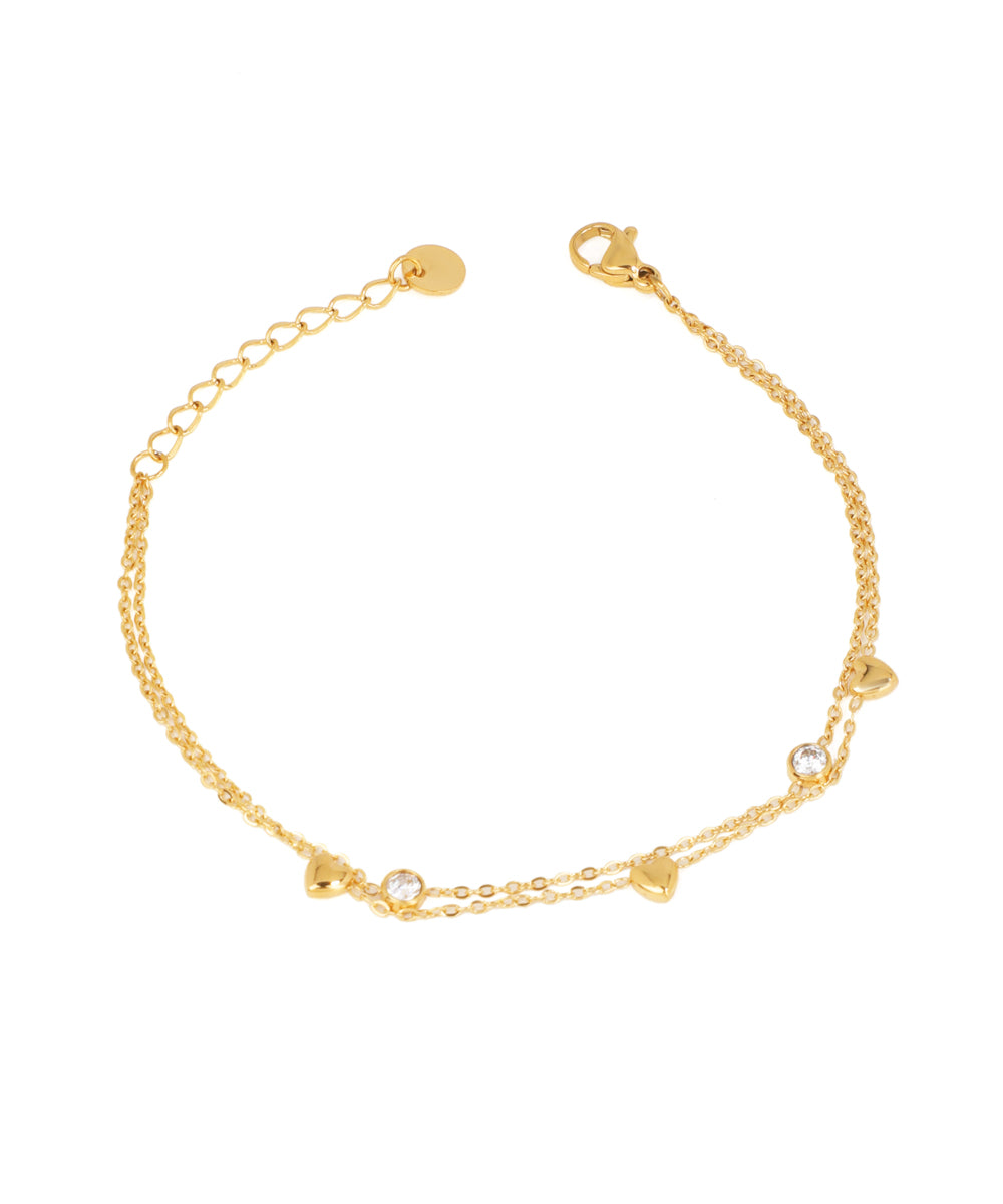 Gold-tone layered chain bracelet with small heart charms and round bezel-set clear stones, lobster clasp.