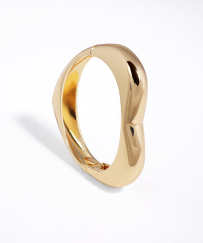 Shiny gold-tone cuff bracelet with a modern sculptural wavy design and hinge closure