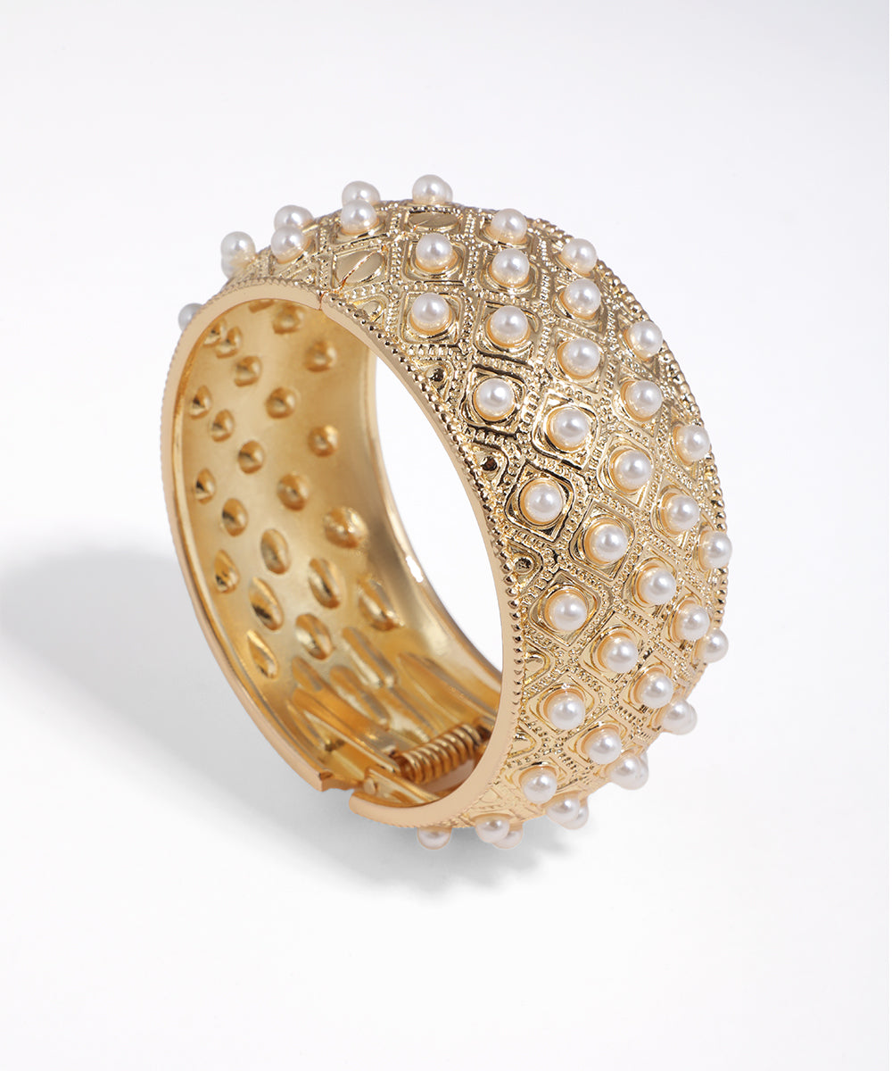 Gold-tone bangle bracelet with intricate diamond pattern and faux pearls.