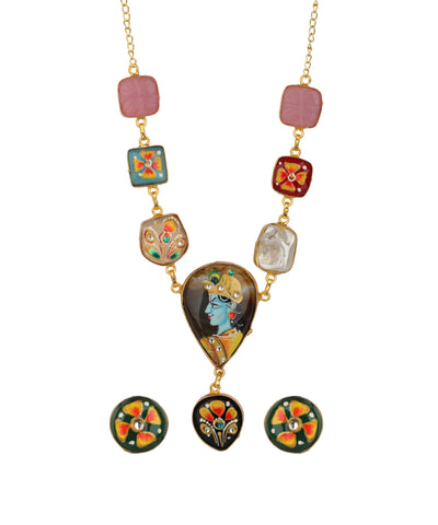 A gold-tone necklace with a large central teardrop pendant featuring a hand-painted illustration of Lord Krishna, flanked by smaller decorative beads and matching circular earrings, shown on a plain white background.
