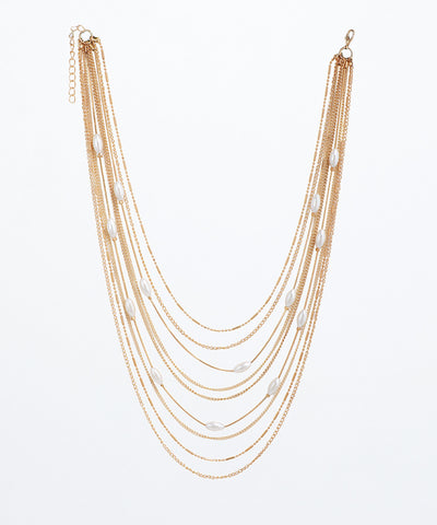 Gold-tone layered necklace with varied chains and interspersed white oval faux pearls, featuring an extender chain.