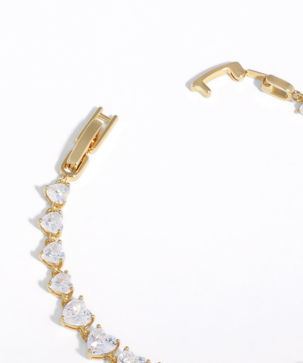 Gold bracelet with heart-shaped clear stones on a white background
