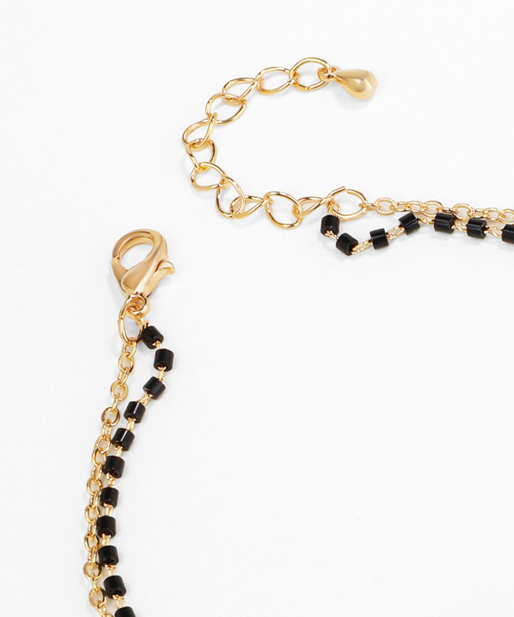 Gold bracelet with black beads on a white background