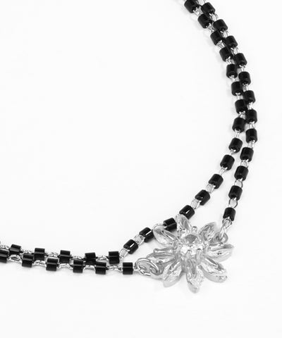 Necklace with black beads and a silver flower pendant on a white background