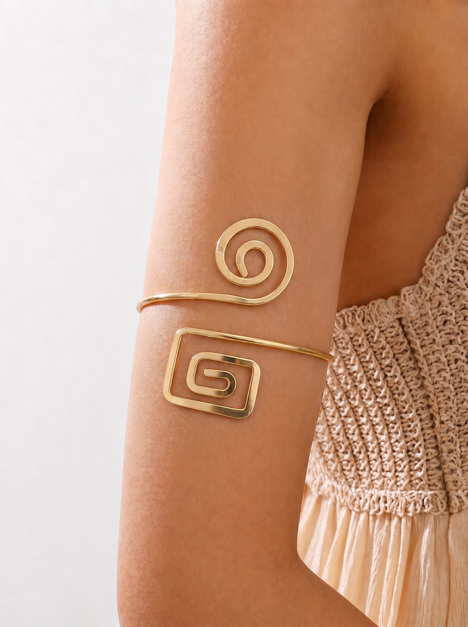 Gold arm cuff with spiral design on a person's arm against a neutral background