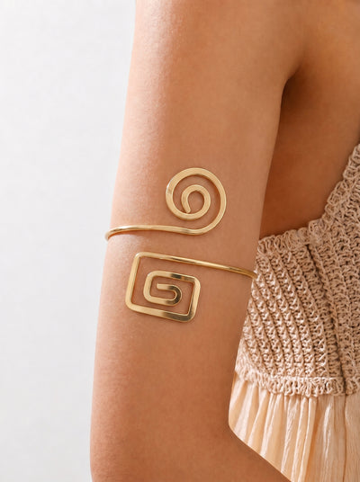 Gold arm cuff with spiral design on a person's arm against a neutral background