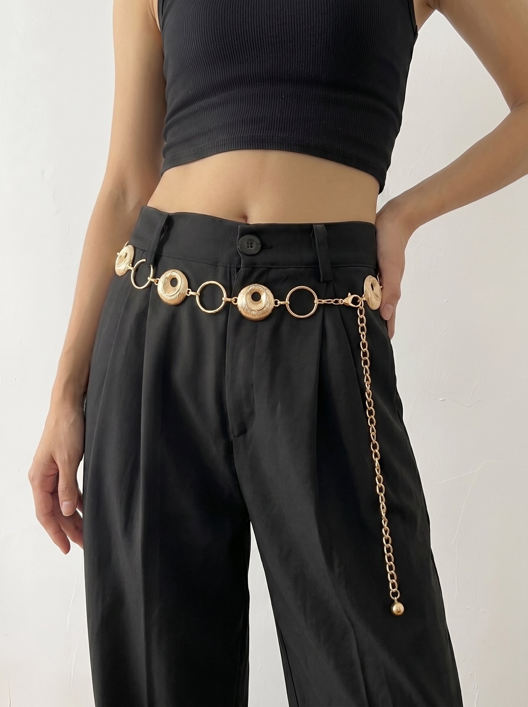 Person wearing black pants with a gold chain belt on a white background