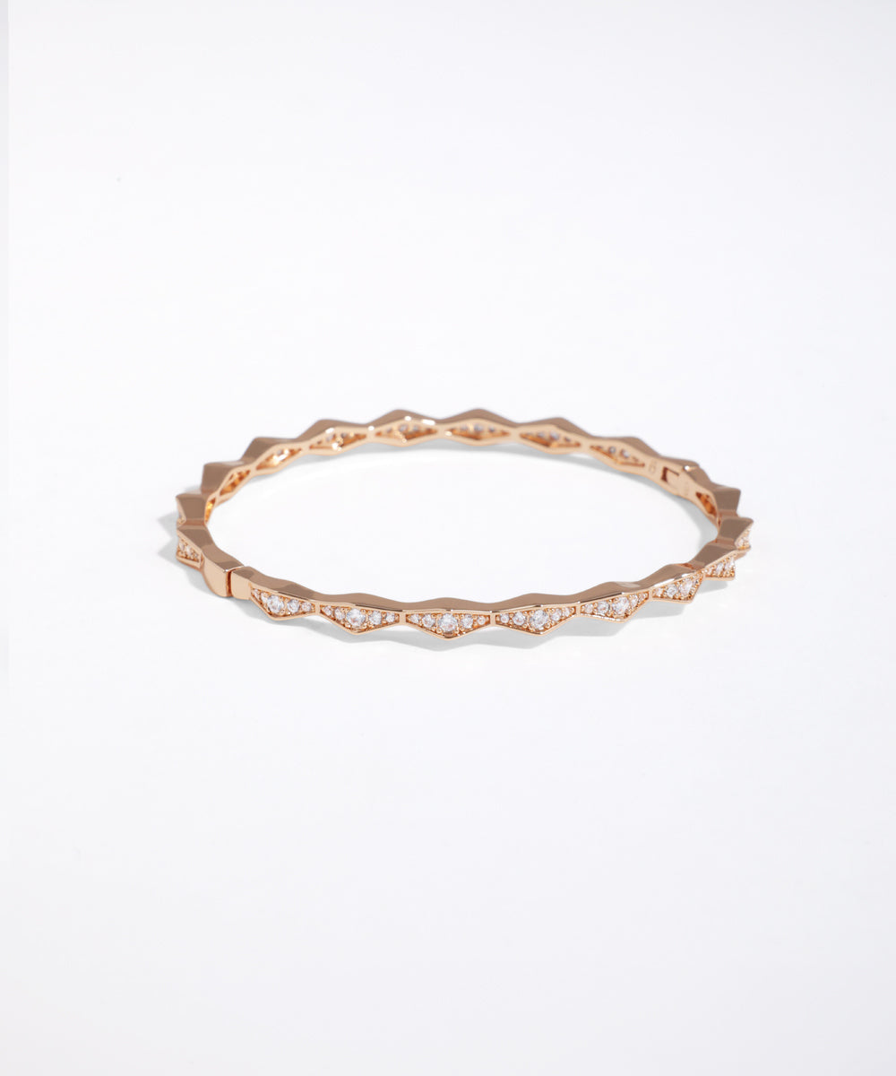 Rose-gold-tone bangle bracelet with geometric faceted edge and clear stone accents.