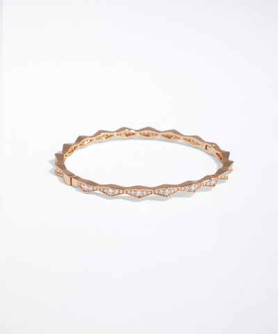 Rose-gold-tone bangle bracelet with geometric faceted edge and clear stone accents.